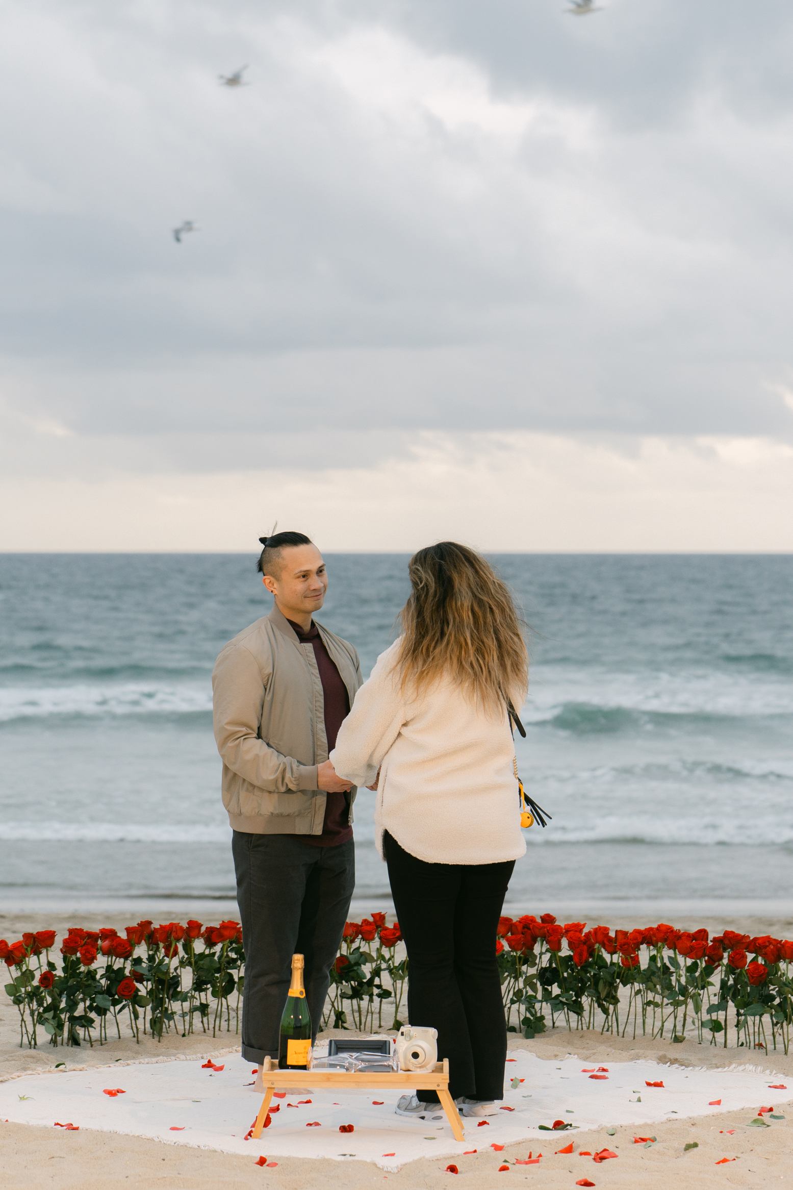 Romantic DIY beach proposal setup with red roses at Venice Beach, California.