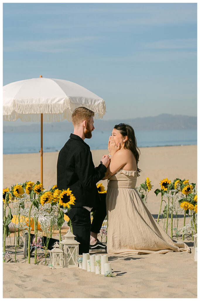 A couple embraces at their beach picnic proposal in Hermosa Beach, Los Angeles.