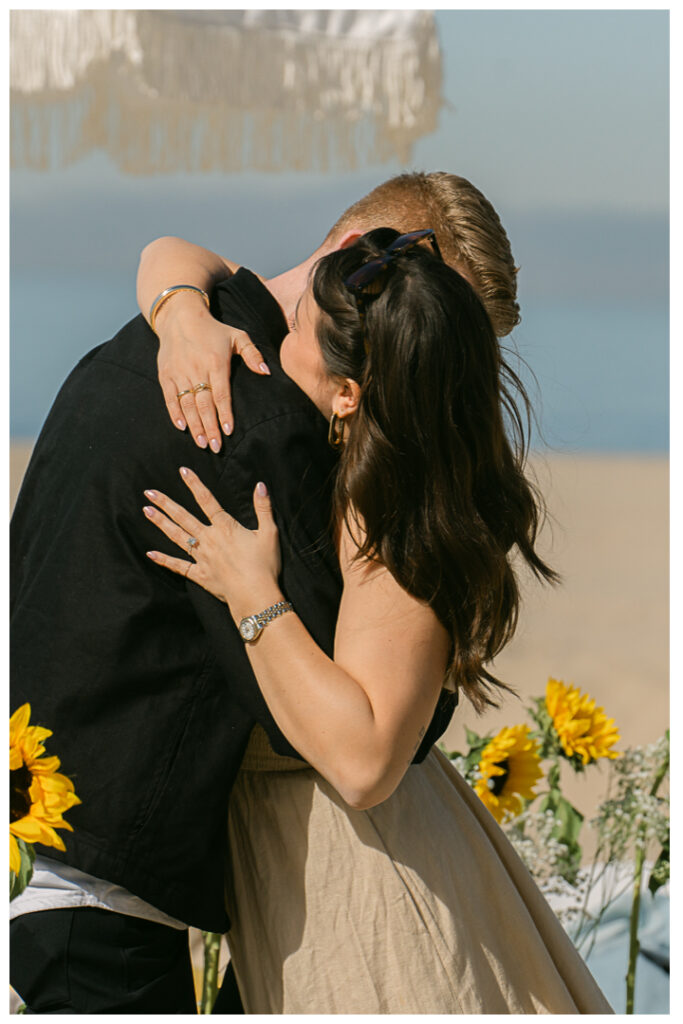 A couple embraces at their beach picnic proposal in Hermosa Beach, Los Angeles.