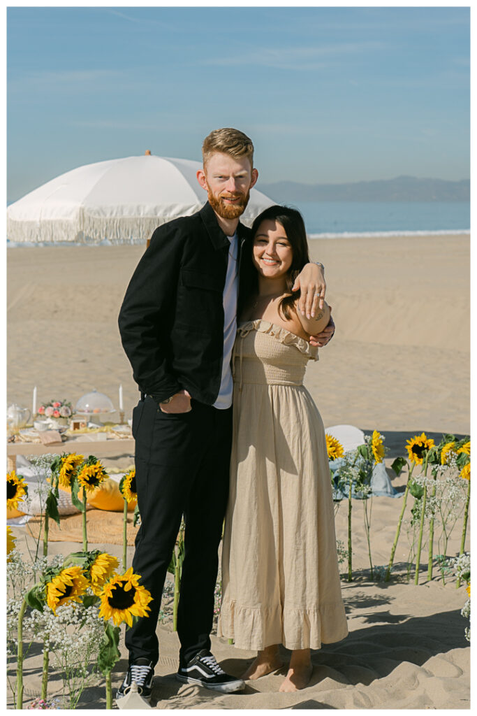 A couple embraces at their beach picnic proposal in Hermosa Beach, Los Angeles.