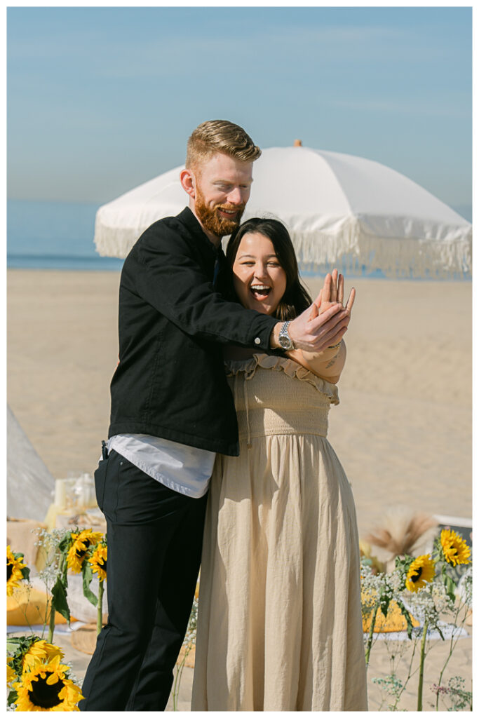 A couple embraces at their beach picnic proposal in Hermosa Beach, Los Angeles.