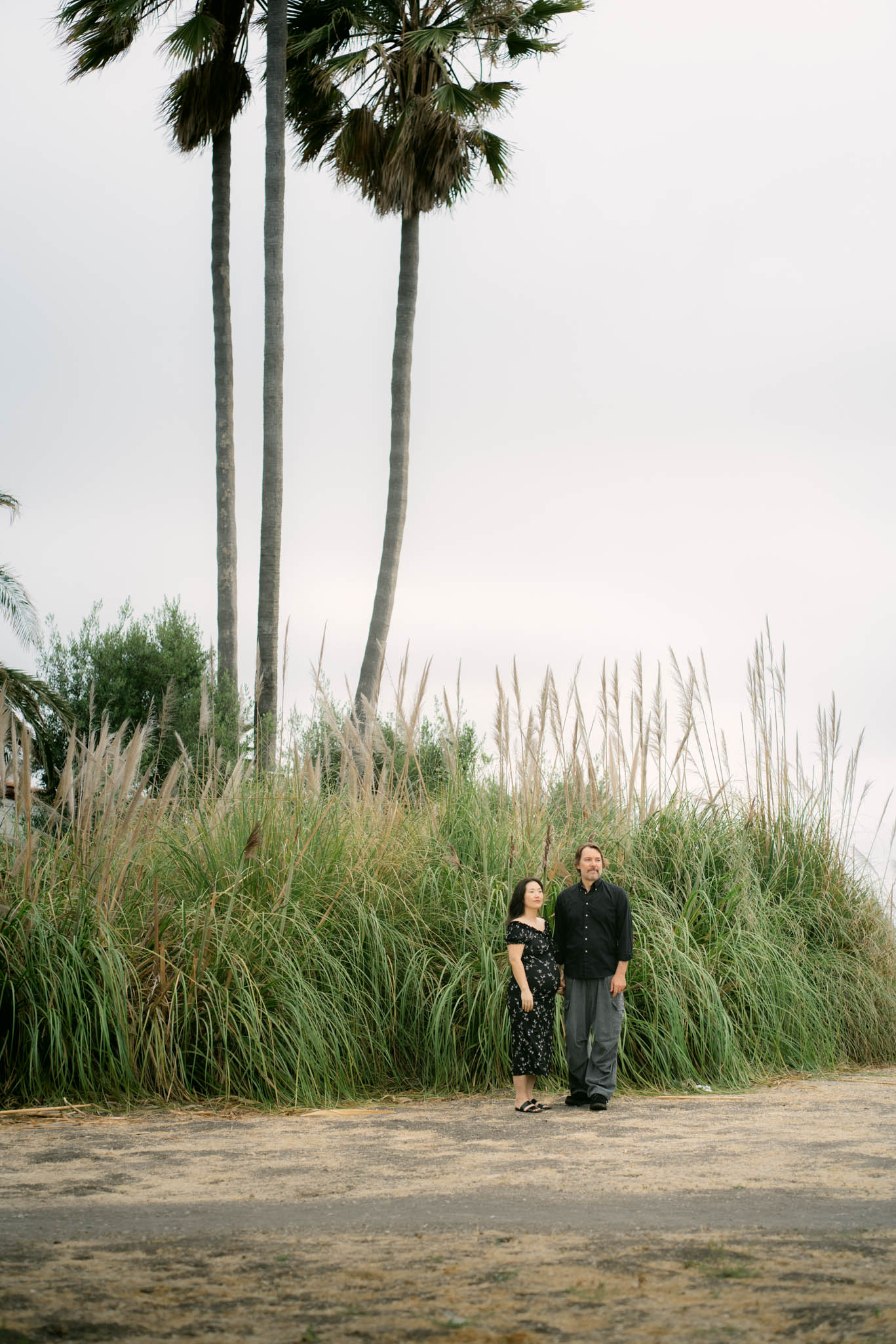 Expecting couple standing near Palos Verdes cliffs during an overcast maternity photoshoot with soft coastal light.