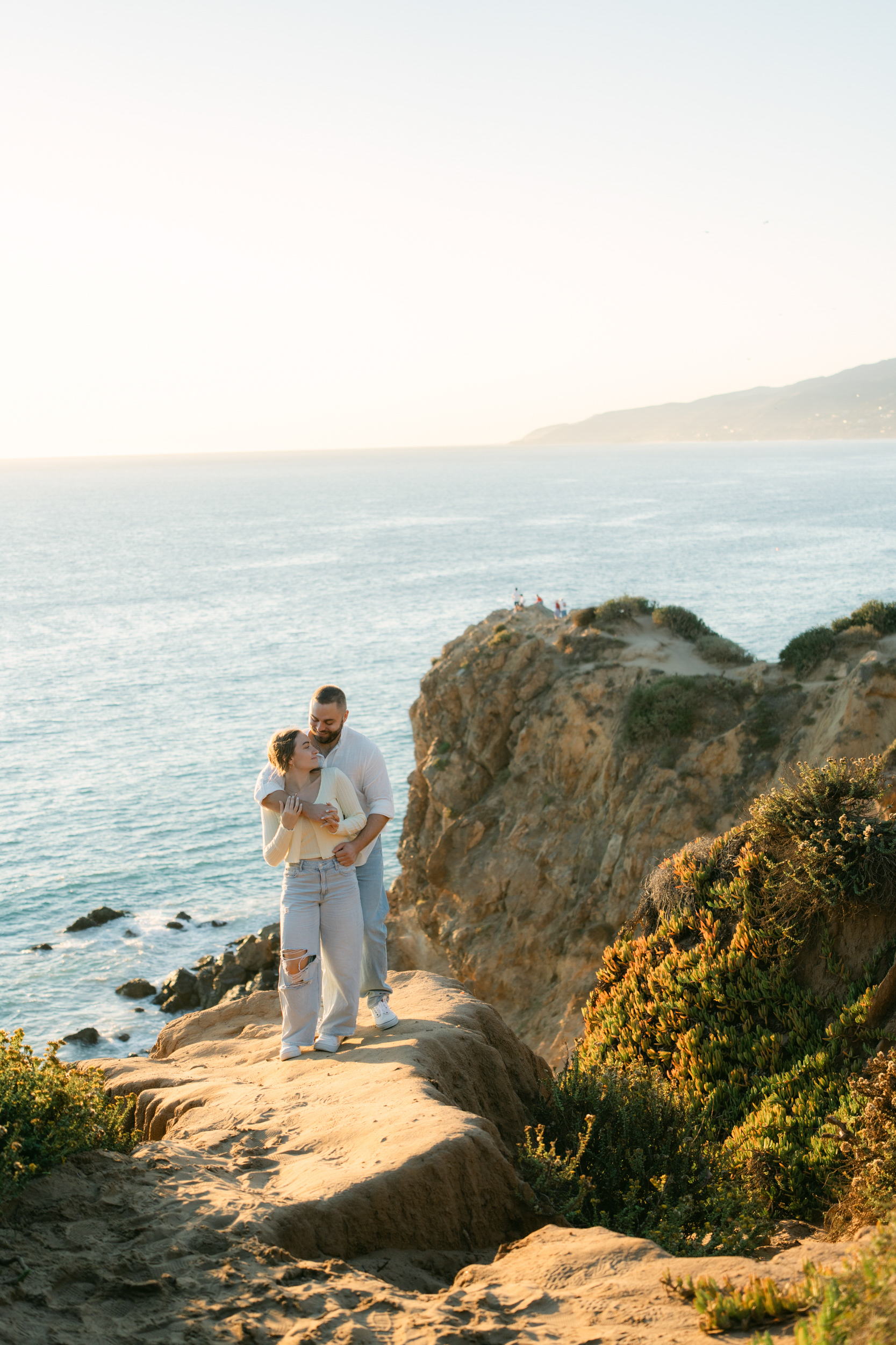 Surprise proposal at Point Dume in Malibu with a couple embracing on a cliffside overlook at golden hour