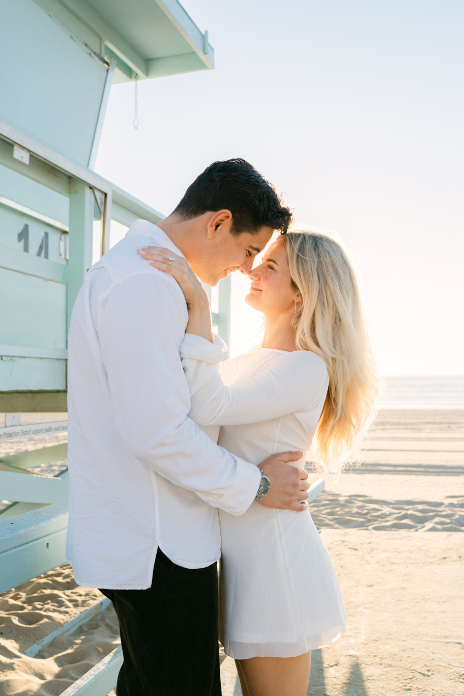 Wide scenic view of a Manhattan Beach surprise proposal with pastel sunset sky and lifeguard tower in the background