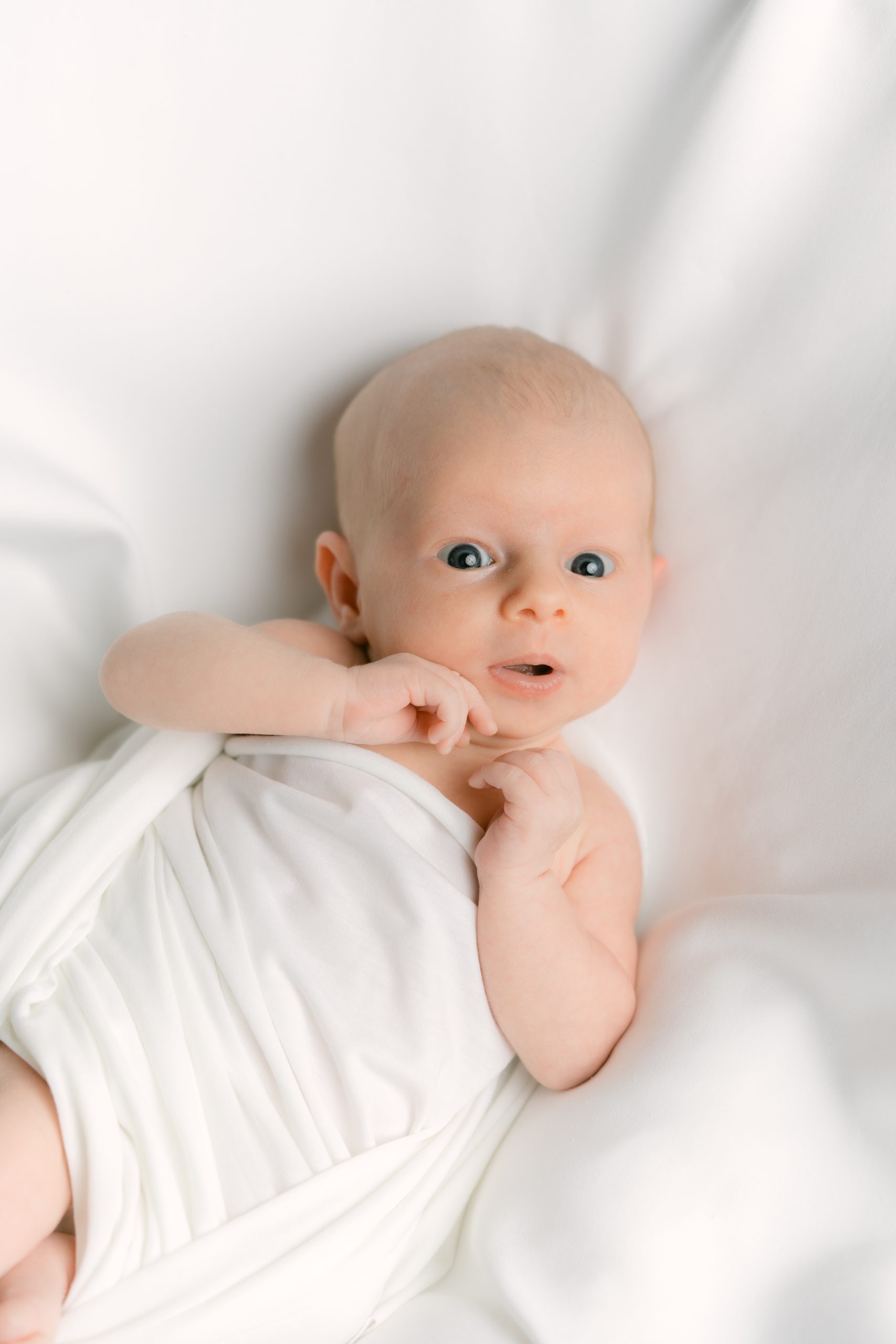 Newborn swaddled in white with one hand raised during an in-home session in Orange County